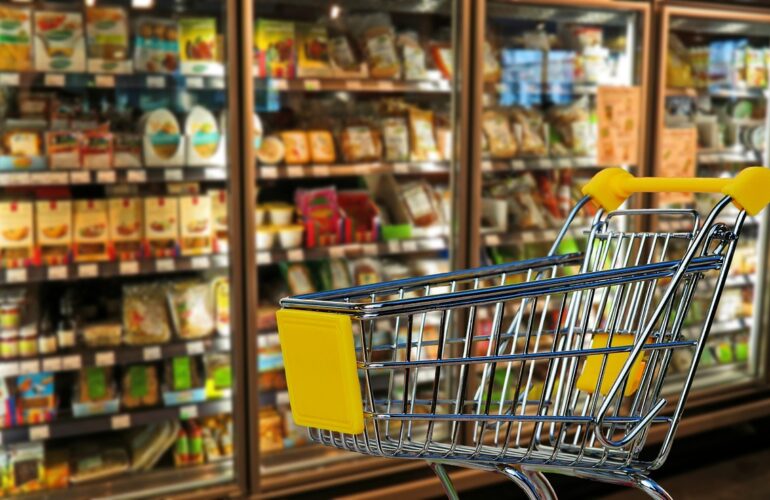 Carrello della spesa con prodotti sullo sfondo